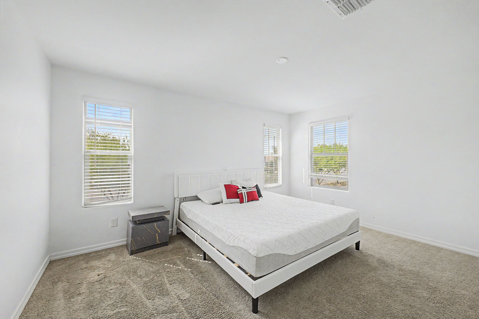 A bedroom with a bed, a nightstand, a dresser, and two windows with blinds.