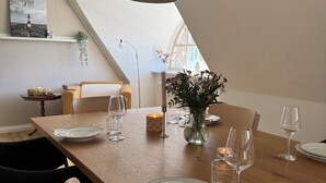 Comedor con mesa de madera para cuatro, un florero con flores e iluminación colgante.