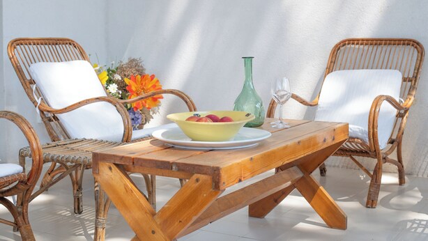 Ein Holztisch mit einer Obstschale, zwei Korbstühle und einer Vase mit Blumen.