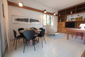 A dining area with a round table, black chairs, a patterned armchair, and a television on a wooden stand. - Villa Montecristo - Diadema di Venere (Marina di Campo)