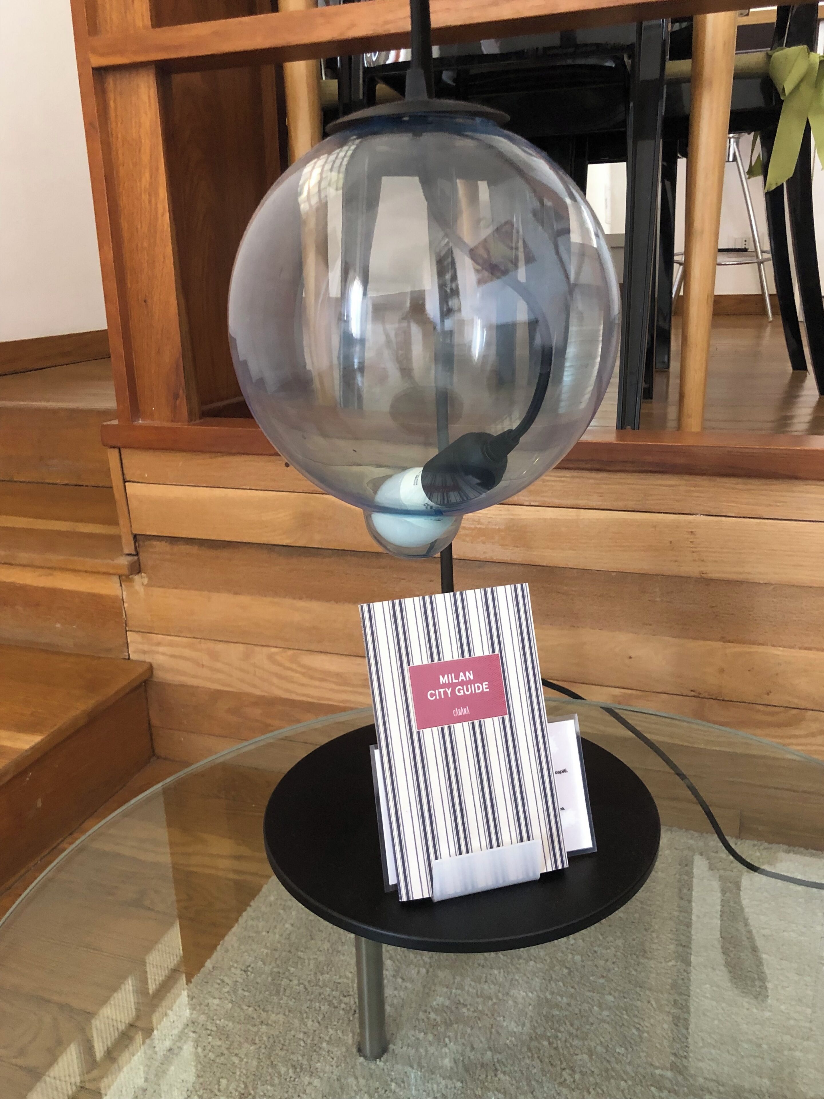Une table en verre sur laquelle sont posés un guide touristique de Milan et un globe terrestre transparent.