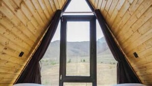 A room with a wooden sloped ceiling, two beds, a large window, and a view of a mountainous landscape. - Your Peaceful Retreat in Kazbegi – Chalet with Stunning Views & Warm Charm (HHWF+JH, Sioni, Georgia)
