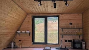 A kitchen with wooden walls, a window, a sink, a microwave, and a dining area with chairs. - Your Peaceful Retreat in Kazbegi – Chalet with Stunning Views & Warm Charm (HHWF+JH, Sioni, Georgia)