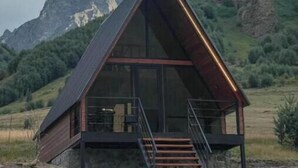 A modern, triangular wooden cabin with a glass facade, set against a mountainous backdrop. - Your Peaceful Retreat in Kazbegi – Chalet with Stunning Views & Warm Charm (HHWF+JH, Sioni, Georgia)