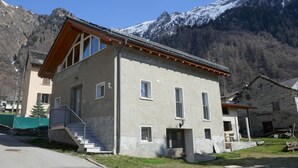 A two-story building with a sloped roof, a staircase leading to the entrance, and a view of snow-capped mountains in the background.