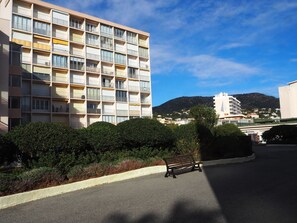 A multi-story hotel with balconies, a parking area, and a mountain in the background. - Les Horizons by Interhome (Le Lavandou)