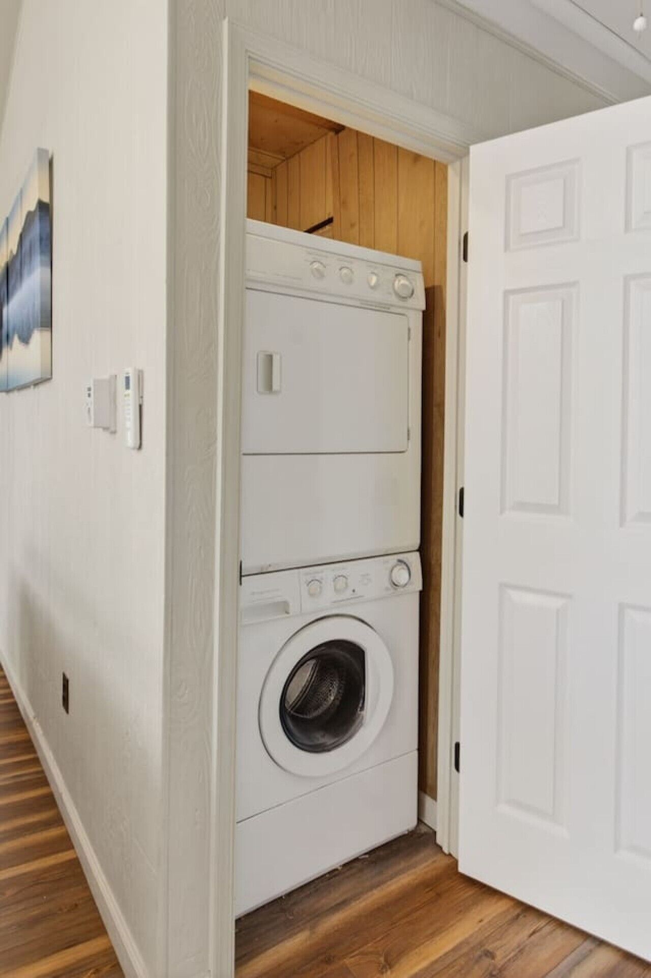 A laundry room with stacked washers and dryers, wooden flooring, and a white door.