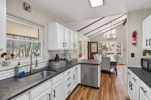 A modern kitchen with white cabinetry, a granite countertop, and a dining area with a wooden table and chairs. - Hot Tub & Fire Pit • 1 Min to Lake (lake harmony)