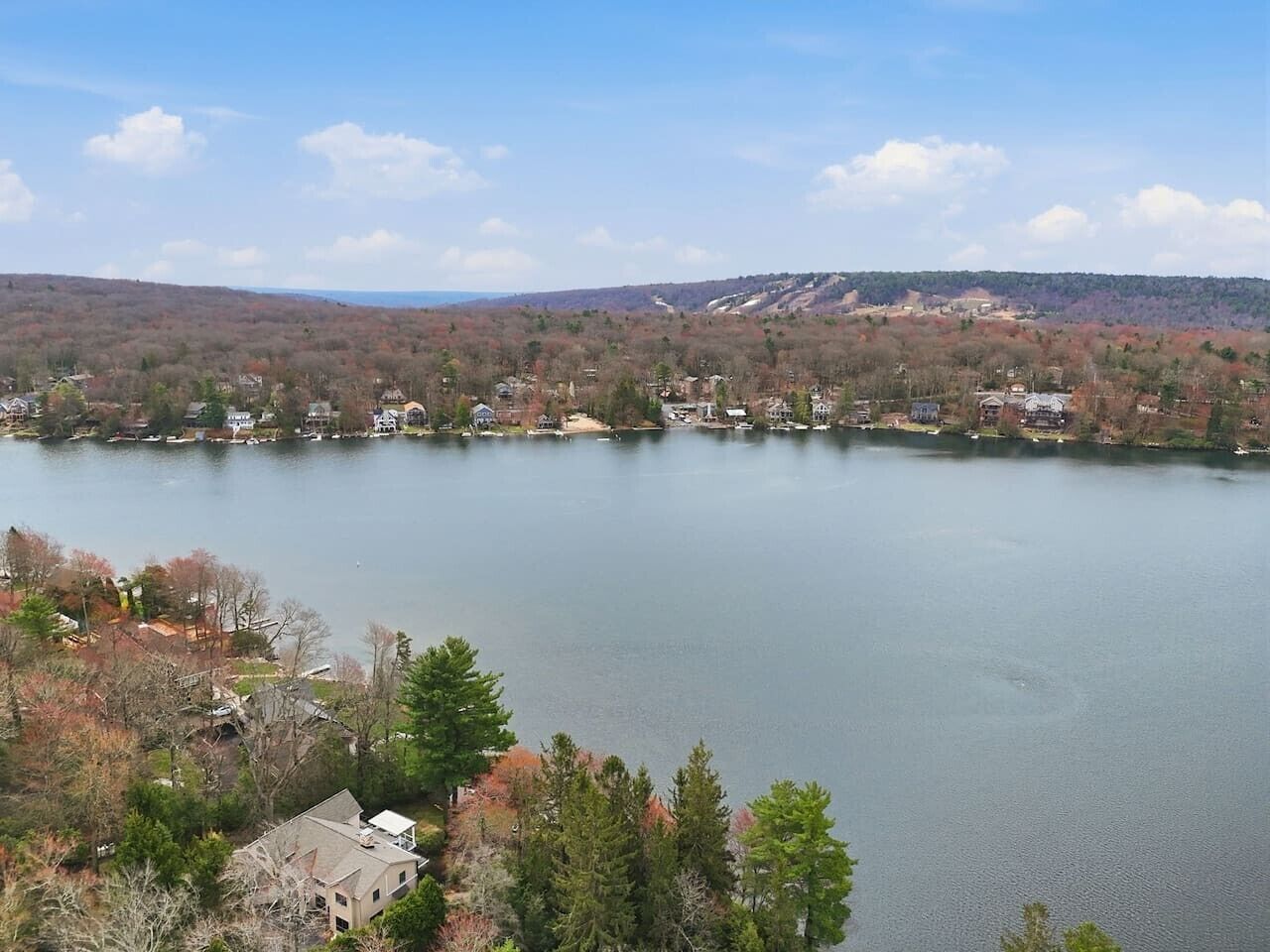 A lake with houses on the shore, surrounded by trees and hills.