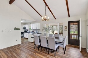 A modern kitchen with white cabinets, a dining area with a table and chairs, and a chandelier. - Hot Tub & Fire Pit • 1 Min to Lake (lake harmony)
