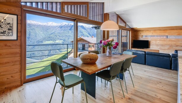 A modern room with a wooden interior, a dining table with chairs, a sofa, a TV, and a large window offering a mountain view. - Chalet Oberjuval – Unique and Stylish Retreat Amidst Alpine Meadows (Castelbello-Ciardes)