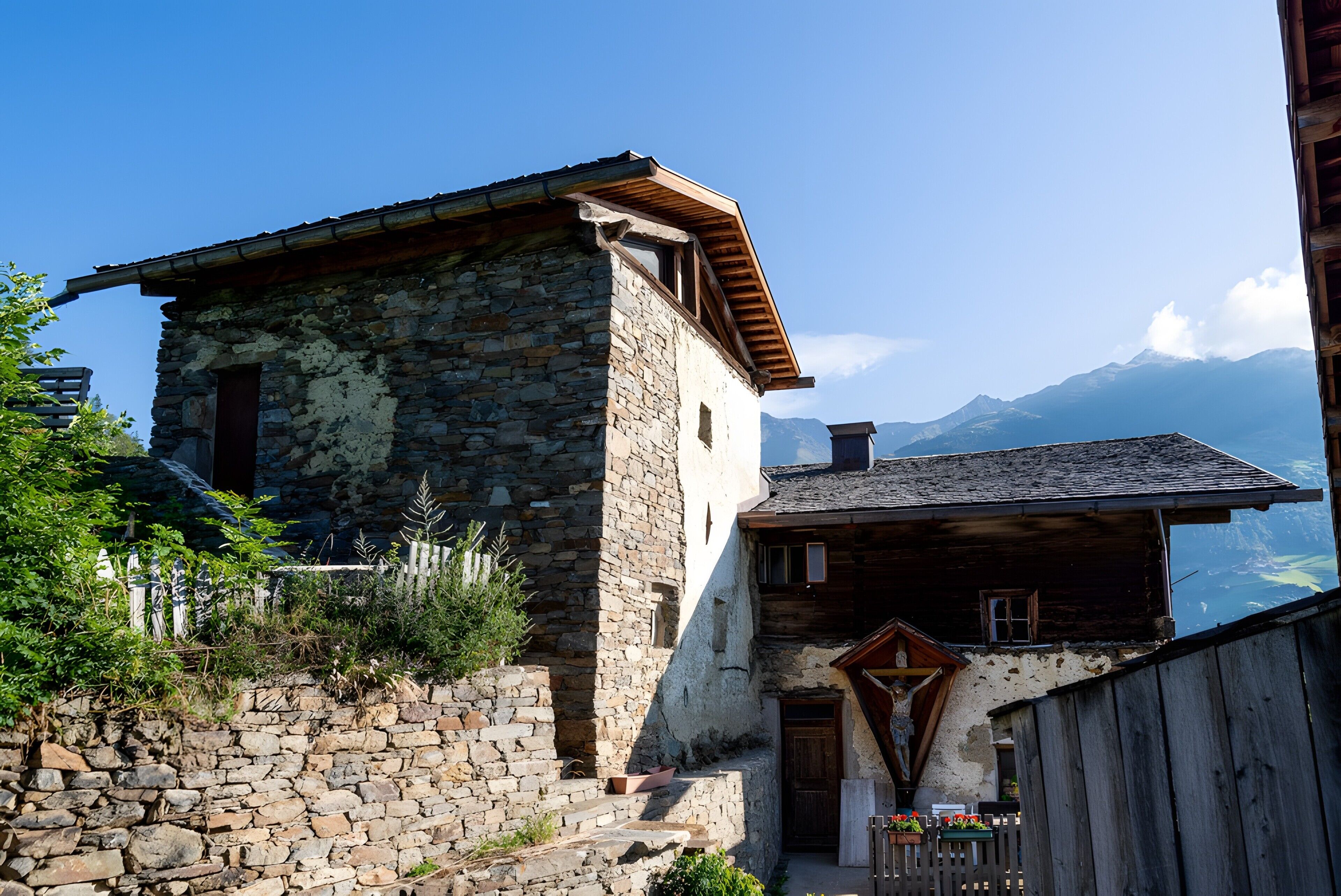 A stone building with a wooden upper section, a wooden door, and a small balcony with flowers.