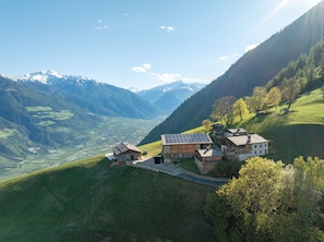 Un paysage montagneux avec des maisons construites sur le flanc d’une colline, une vallée en contrebas et, au loin, des montagnes aux sommets enneigés.