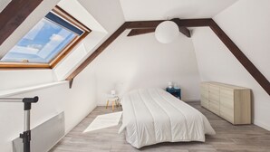 A bedroom with a sloped ceiling, a skylight, a bed, a nightstand, a dresser, and a radiator. - Charming duplex for 2 in the city center (Pont-l´Abbé)