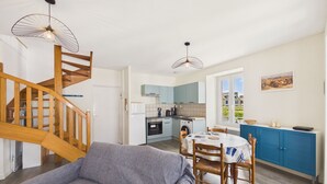 A modern kitchen with a dining area, wooden staircase, and a view of the outside. - Charming duplex for 2 in the city center (Pont-l´Abbé)