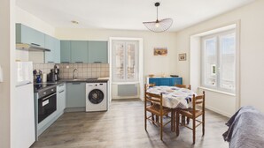 A compact kitchen with a washing machine, a dining area with a table and chairs, and a large window. - Charming duplex for 2 in the city center (Pont-l´Abbé)