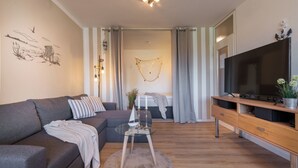 En moderne stue med sofa, fjernsyn og en pyntende plante.
