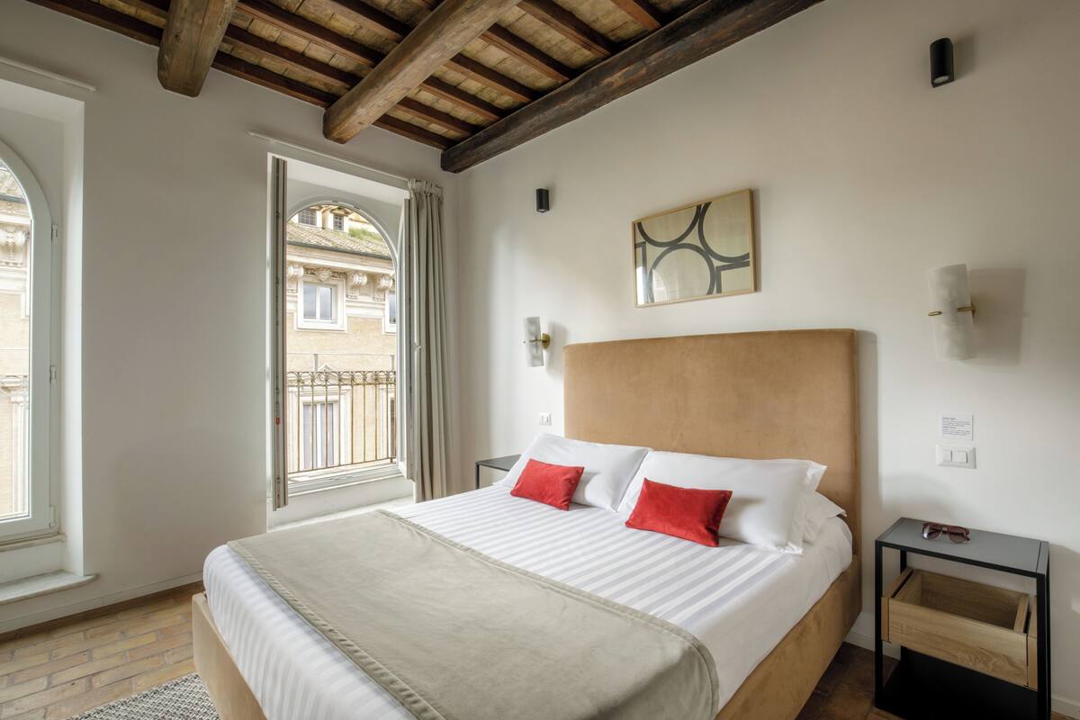 A bedroom with a large bed, a wooden headboard, a nightstand, and a window with curtains.
