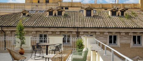 Una terraza en la azotea con mobiliario exterior, una planta en maceta y vistas de los edificios circundantes.