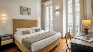 A hotel room with a bed, bedside table, lamp, chair, and a view of the city through large windows. - Signature Rooms by Hannah Hotels Collection (Rome)