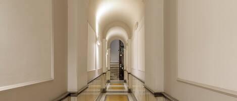 Um corredor comprido e estreito com piso de mármore e paredes brancas.