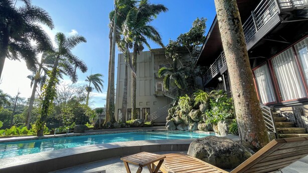 A poolside area with lounge chairs, a wooden table, and a building with balconies. - Tagaytay Haven Ulat Managed by Novella (Tagaytay)