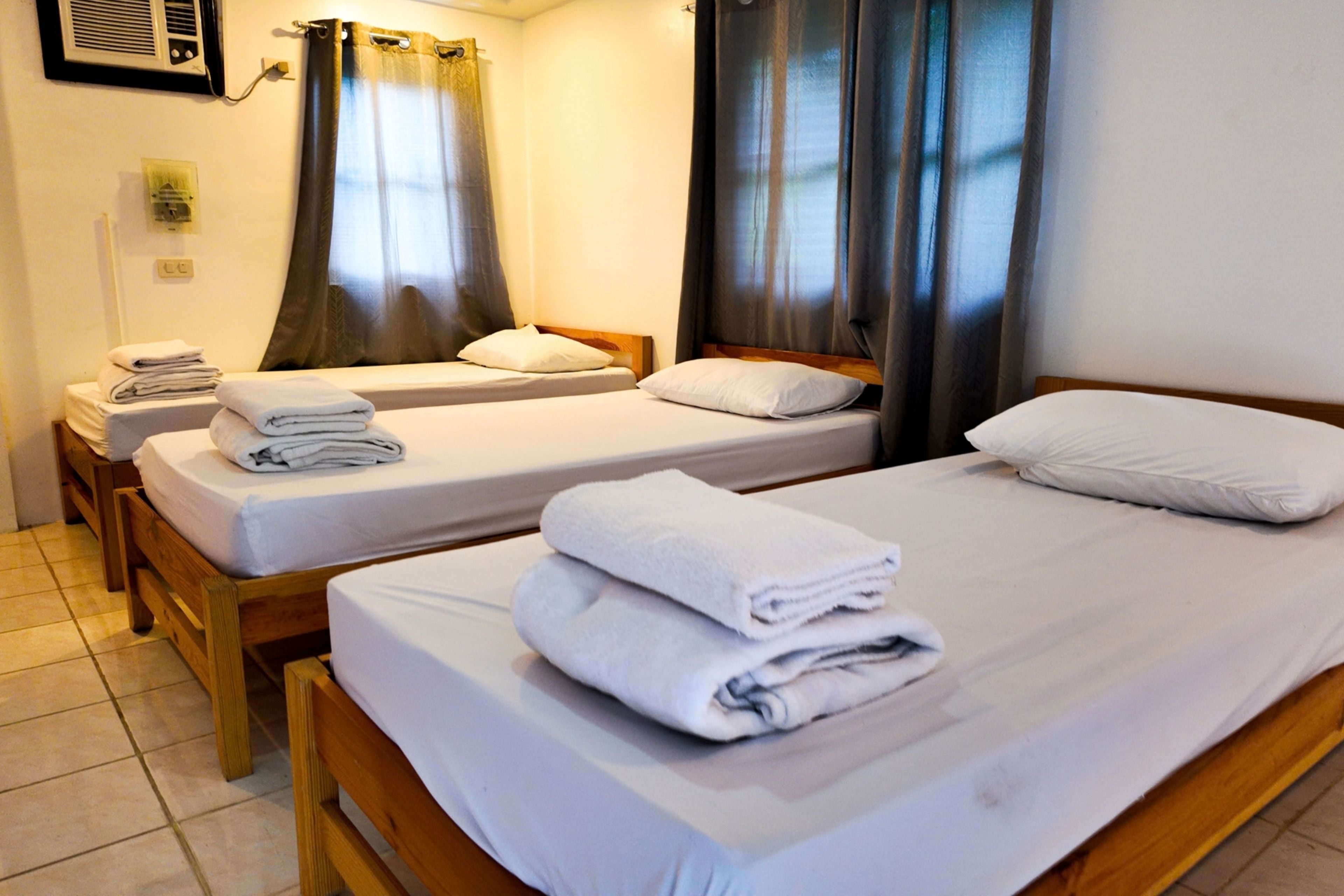 A hotel room with two single beds, each with a neatly folded white towel and a pillow.