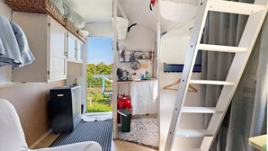 A compact room with a bed, a small TV, a kitchenette, and a view of greenery. - Bauwagen 'Natur Pur/No.7' with Private Terrace and Panoramic Countryside Views (Ötisheim)