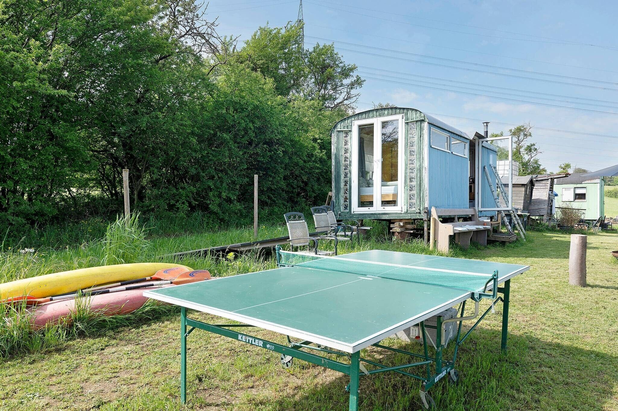 Una mesa de ping pong verde, kayaks y una casa móvil azul en una zona con césped.