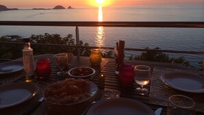 Ein Esstisch, gedeckt für ein Abendessen, mit Blick auf das Wasser bei Sonnenuntergang.
