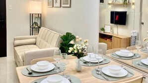 Ein moderner Essbereich mit Holztisch für vier Personen, einer Couch und einem an der Wand montierten Fernseher.