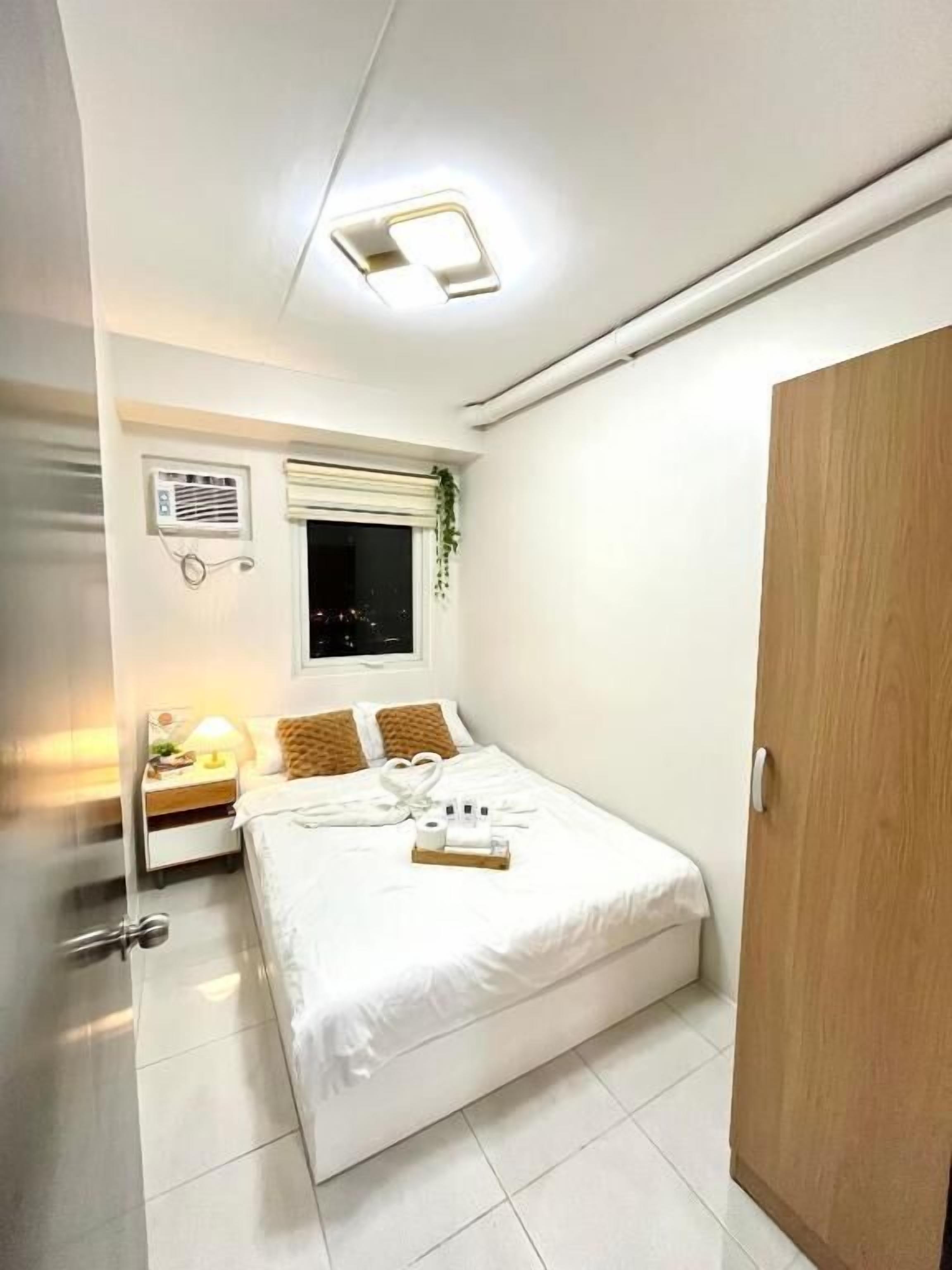 A bedroom with a bed, bedside table, lamp, window, and a wooden wardrobe.