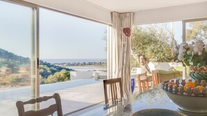 Un comedor con mesa de vidrio, sillas y vistas a un paisaje con árboles y un cuerpo de agua.