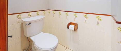 A bathroom with a toilet, a towel dispenser, and a framed certificate on the wall.
