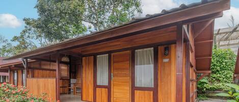 A wooden building with a covered porch, a small staircase, and a garden area with plants and a water feature.