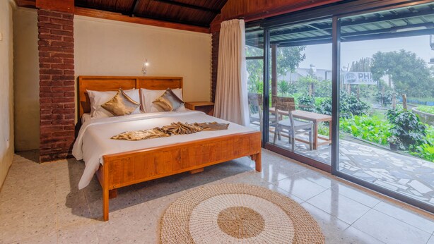 A bedroom with a wooden bed, a brick wall, and a large sliding glass door leading to a patio. - Kampung Bingo Glamping & Resto (Baturiti)