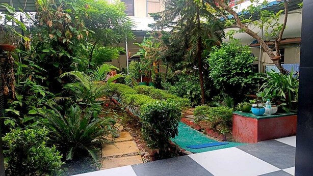 A lush garden with a stone pathway, potted plants, and a small water feature. - Homestay Urmil Basant (Jaipur)