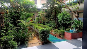 A lush garden with a stone pathway, potted plants, and a small water feature.