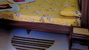 A bed with floral bedding, a wooden headboard, a bedside table, and decorative wall patterns. - Homestay Urmil Basant (Jaipur)