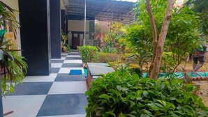 A courtyard with a checkered floor, potted plants, and a covered seating area. - Homestay Urmil Basant (Jaipur)