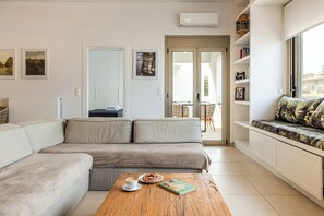 Una sala de estar moderna con un sofá modular, una mesita de centro con un libro y un pretzel, y vistas al exterior a través de un ventanal.