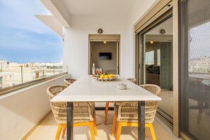 Un balcón con una mesa de comedor, sillas de mimbre, un cuenco de fruta y un televisor al fondo.