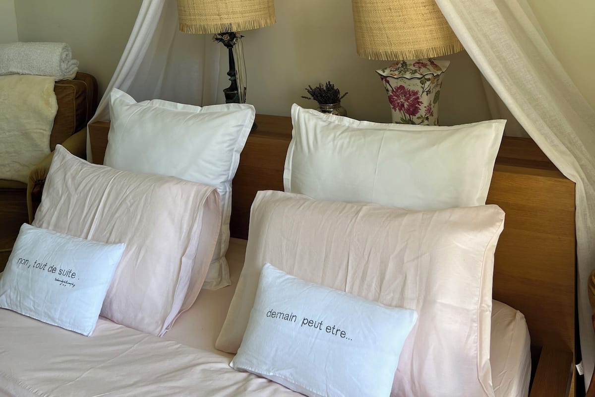 Un dormitorio con cama con dosel, dos lámparas de noche, aire acondicionado de pared y un arreglo decorativo.