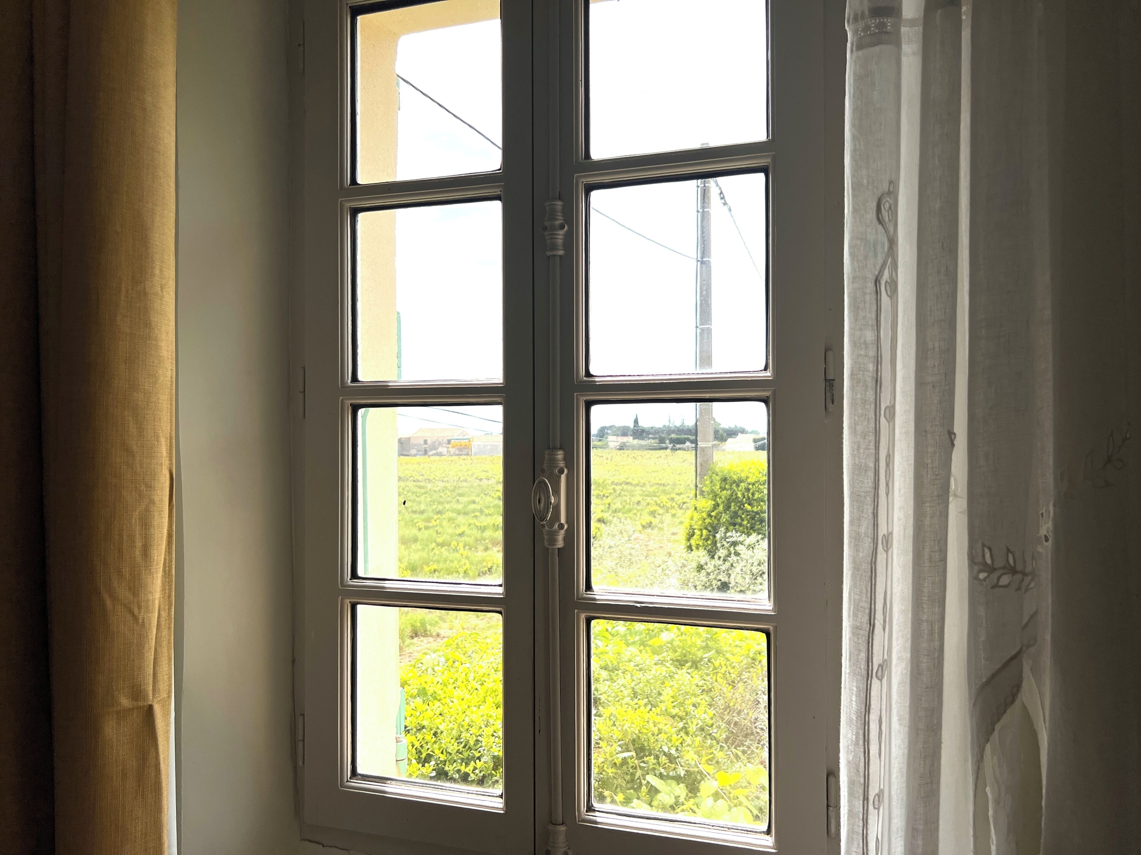Una habitación con un ventanal grande, cortinas y vistas a un campo verde.