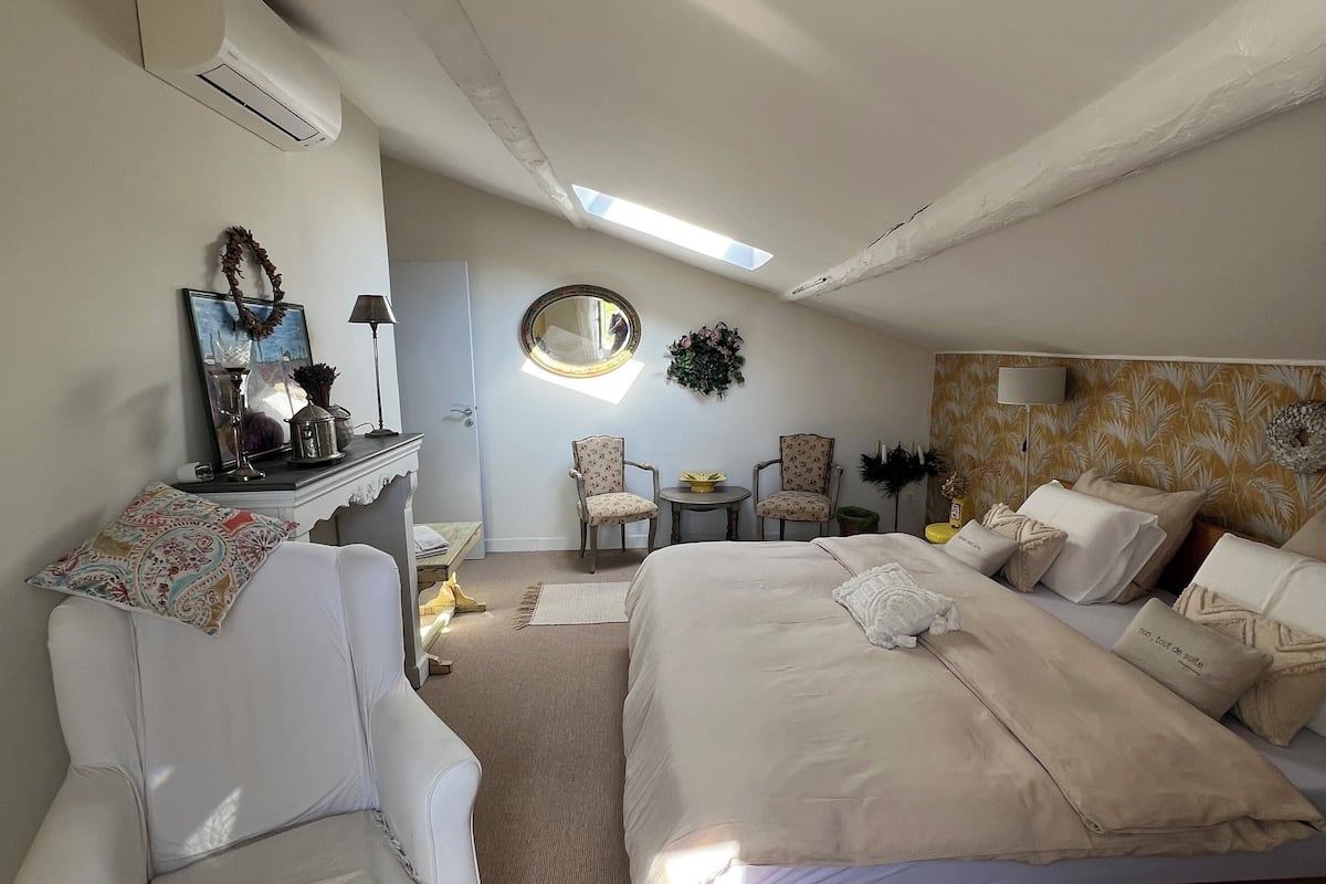 Un dormitorio con cama, dos sillas, una mesita, un espejo y aire acondicionado instalado en la pared.