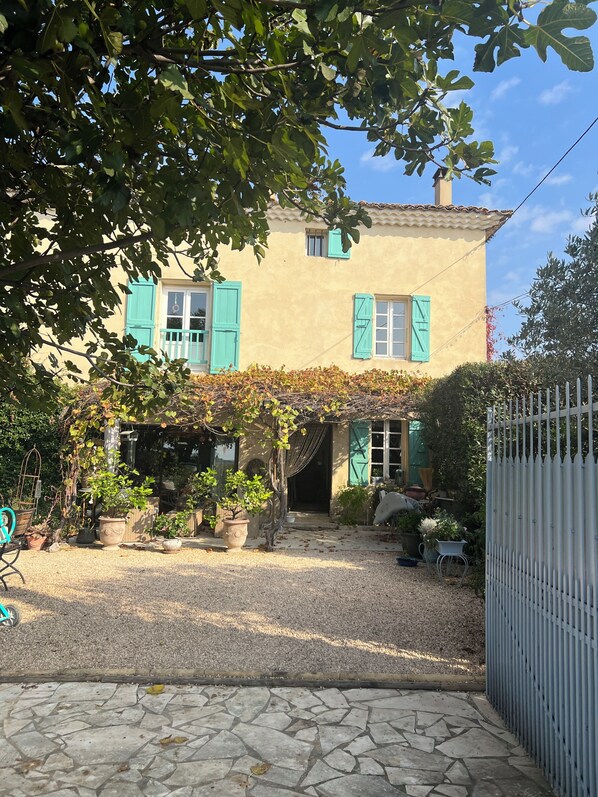A two-story house with a garden, a gravel driveway, and a white fence. - Mas l'Epicure (Vacqueyras)