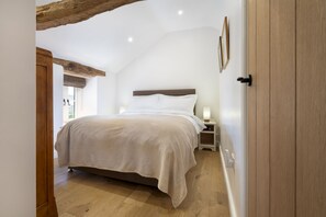 A bedroom with a bed, bedside tables, and a wooden ceiling beam. - Garden Cottage -  Cosy Cottage in Brigsteer (Brigsteer)