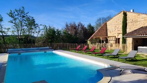 Una piscina con sillones de descanso y un edificio de piedra al fondo.