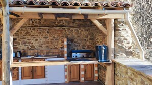 Cocina con pared de piedra, una parrilla empotrada, armarios de madera y piso de baldosas.