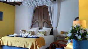 Un dormitorio con cama, cabecera de madera, mesita de noche, lámpara y un florero con flores.